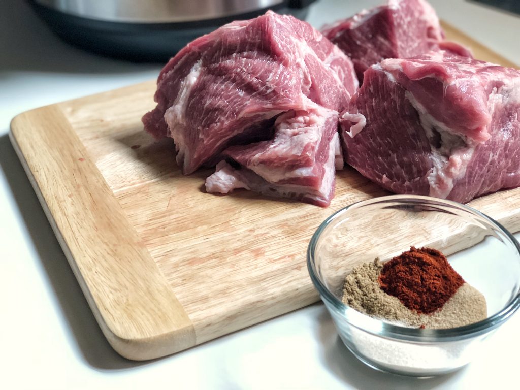 Pork on cutting board near Instant Pot and bowl of spices
